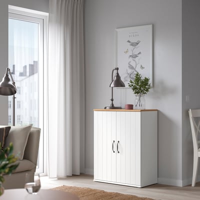 A cosy living room featuring a white SKRUVBY cabinet with double doors, oak top, and black decor. Balanced with a window and chair.