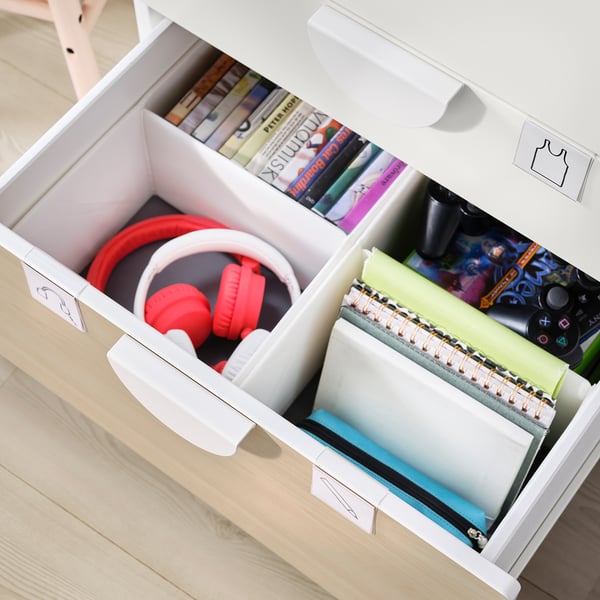 Open white kids drawer showing red headphones, books, and notebooks with illustrations.
