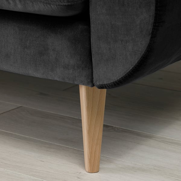 A close-up of a dark grey velvet sofa with wooden legs.