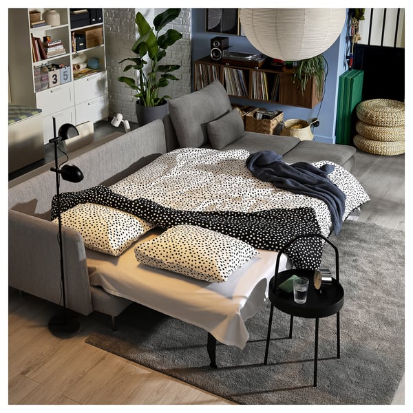 Cosy living room with grey SÖDERHAMN sofa-bed, black side table, patterned pillows, and plants.