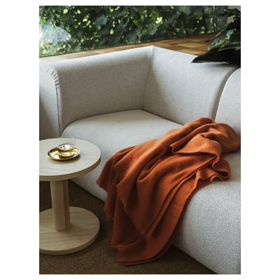 Modern cream sofa with orange blanket, side table, greenery.