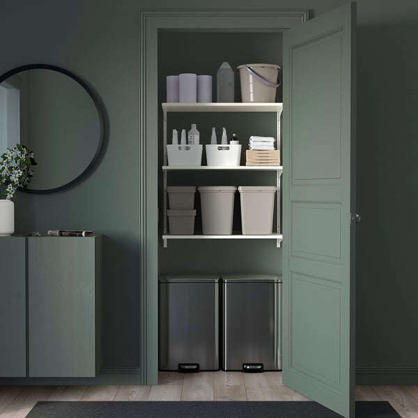 Neat, organised shelf unit in white metal with plastic bins, bottles, and cleaning tools; fits under green counter within a decorations room.