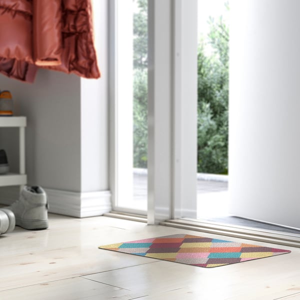 Brightly coloured TORGPLATS doormat by entrance, small, geometric pattern, white wood floor, pairs with red curtain.