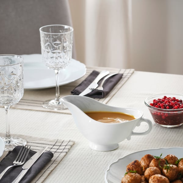 Elegant table setting with porcelain gravy boat filled with sauce, accompanied by plates, glasses, and cutlery neatly arranged for dining.