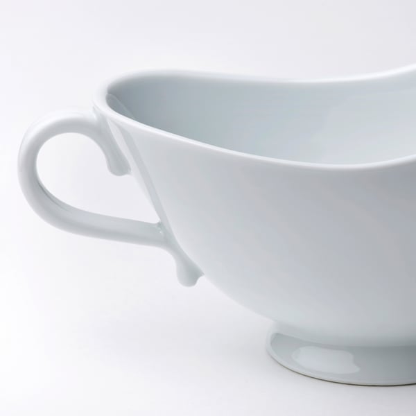 Close-up of white porcelain gravy boat with smooth handle and ruffled edge.