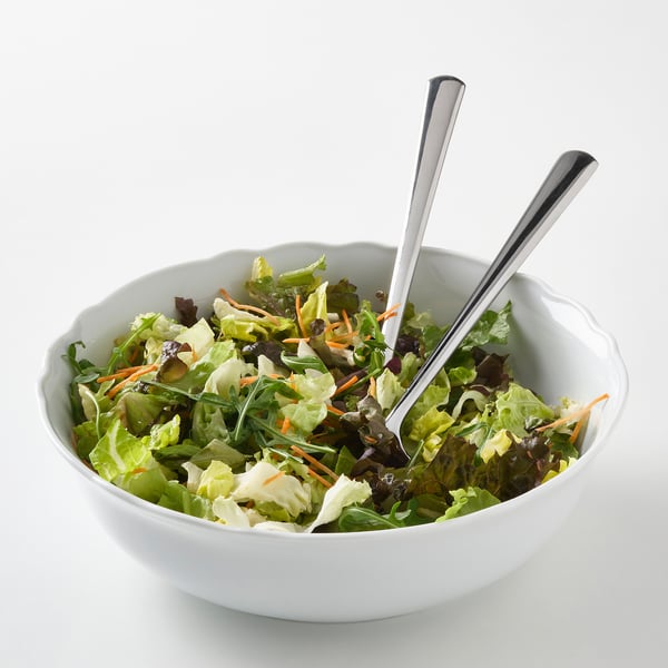 White porcelain bowl with ruffled edge, filled with salad. Two serving spoons stick out of it. Lightweight, durable, dishwasher-safe.