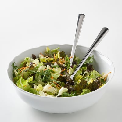 White porcelain bowl with ruffled edge, filled with salad. Two serving spoons stick out of it. Lightweight, durable, dishwasher-safe.