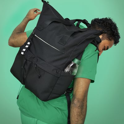 Person with large black recycled polyester backpack, multiple compartments, padded straps, side pockets, striped key chain.