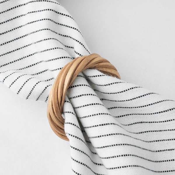 Four handwoven rattan napkin rings arranged on a white tablecloth with black stripes.