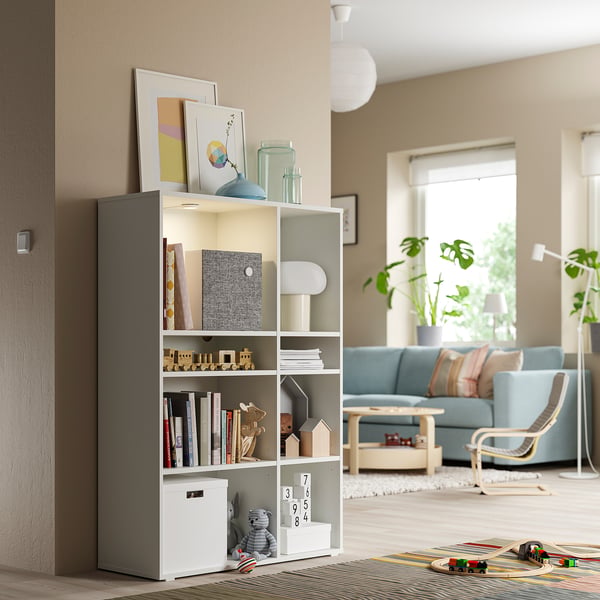 Cosy living room with a VIHALS white shelving unit, holding books, toys, and decor. Light blue sofa, wooden coffee table, and plants are visible.