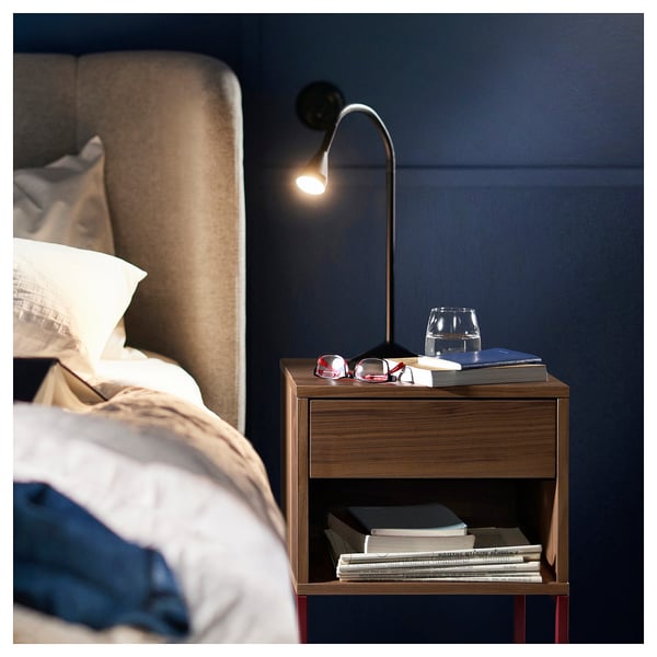 Walnut bedside table VIKHAMMER with drawer, shelves, lamp, books, and glass beside bed.