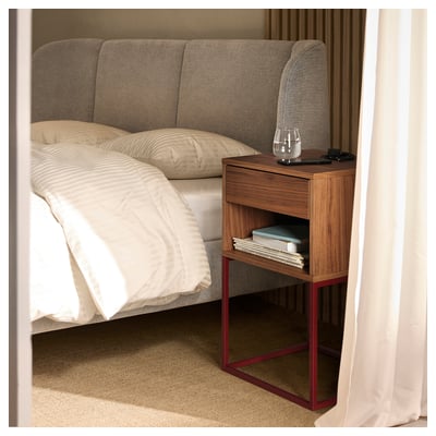 Bedside table named VIKHAMMER with walnut veneer and red steel frame. It has a drawer and open shelf, styling a cosy bedroom.