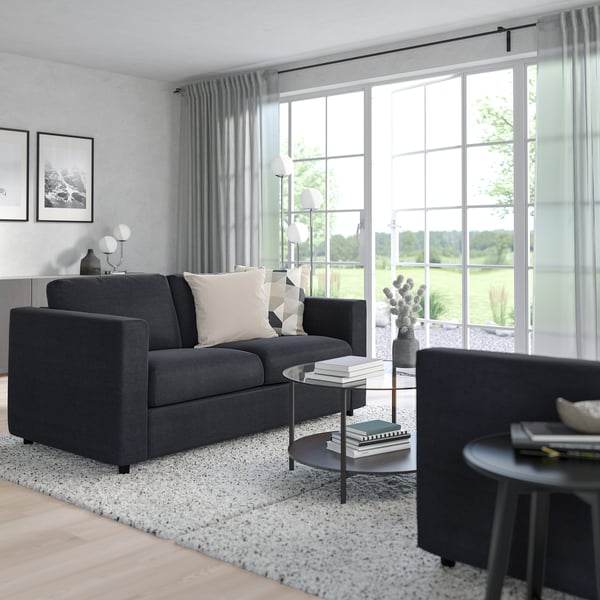 Modern grey sectional sofa with white cushions, armchair, side table, and floor lamp by large windows.