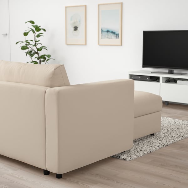 Modern living room with beige VIMLE sectional sofa on wooden floor, flat-screen tv on stand, framed wall art, and potted plant.