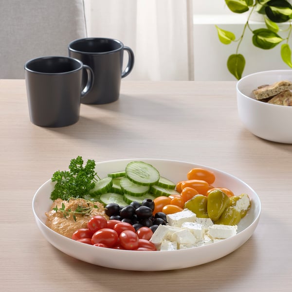 White glass plate with veggies, beside two dark mugs and a bowl of crackers.