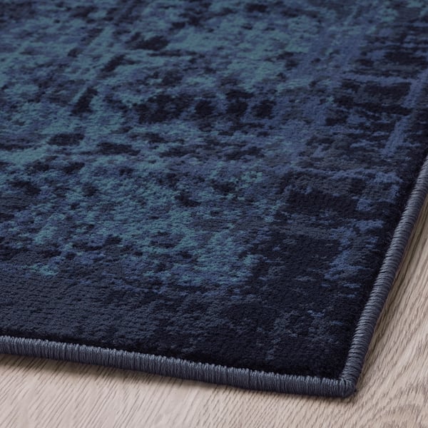 Dark blue area rug with subtle patterns, folded over edge, displaying durable pile.
