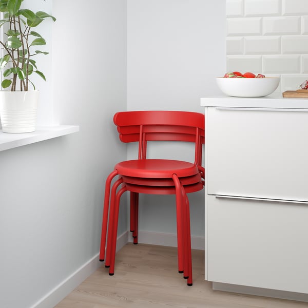 Bright red stackable chair against kitchen wall, next to cabinet and bowl of fruit.
