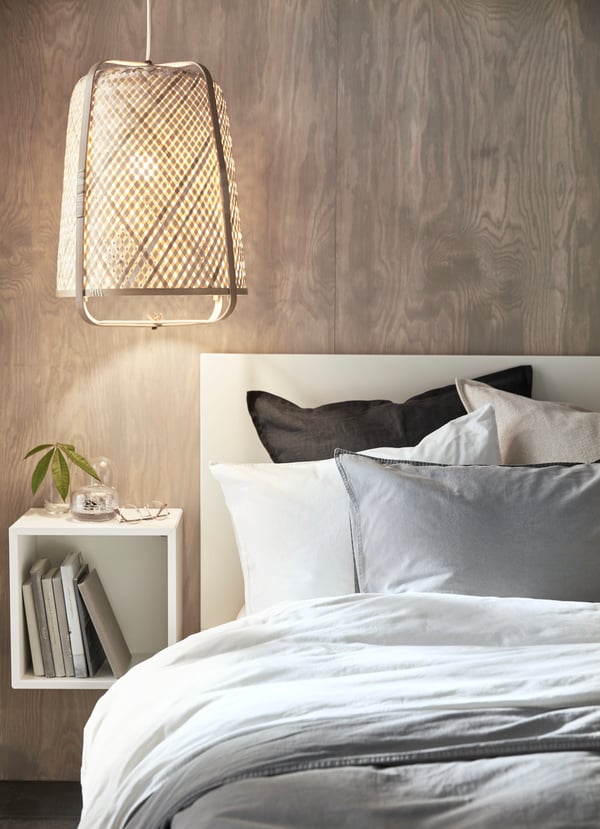The corner of a MALM bed with gray ÄNGSLILJA duvet cover. An EKET wall-mounted shelving unit is placed by the bed.
