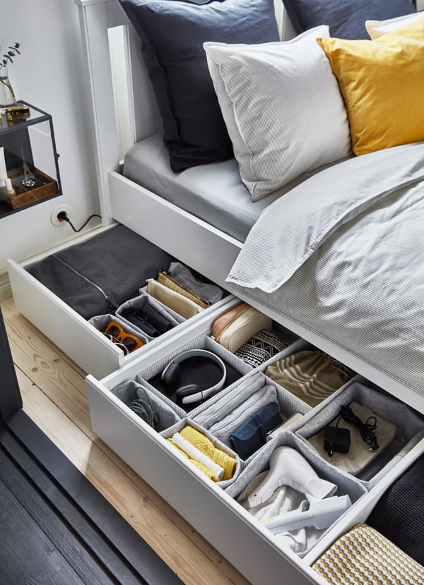 Unter einem Bett liegen kleine Schubladen mit Kleidung darunter mit Organizer.