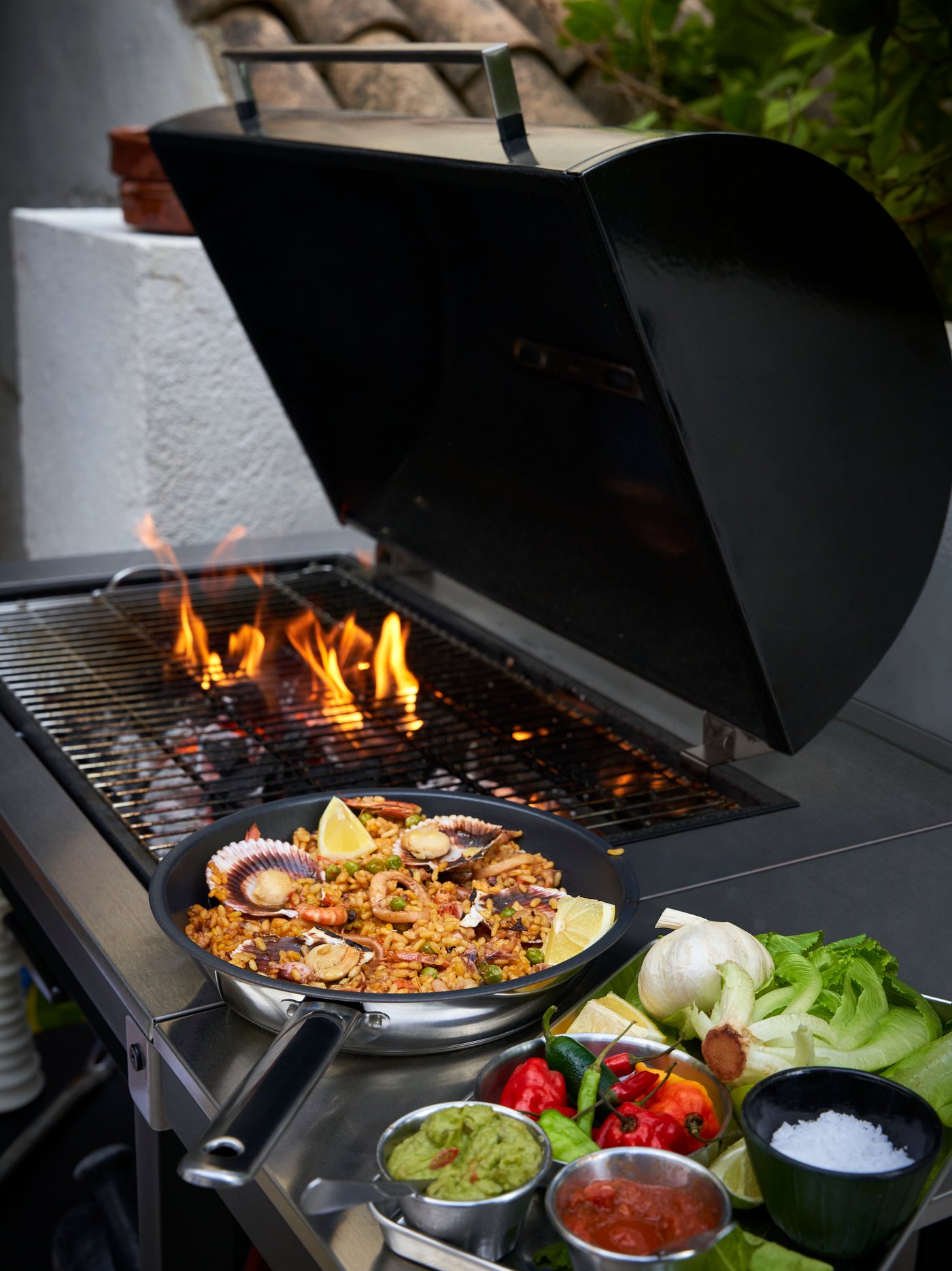 Barbecue à charbon de bois GRILLSKÄR en acier inoxydable avec table d’appoint et poêle IKEA 365+ remplie de paella. 