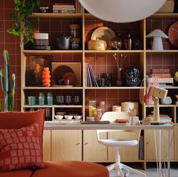 Installée près d’un mur brun-rouge, combinaison de rangement à base d’éléments LÅDMAKARE à portes coulissantes dont les tablettes sont garnies de divers objets.
