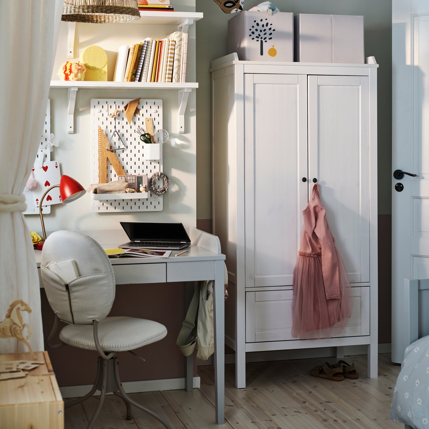 Ein weisser SUNDVIK Kleiderschrank steht in einem Kinderzimmer neben einem grauen SMYGA Schreibtisch mit einem Regal darüber und einem BJÖRKBERGET Stuhl.