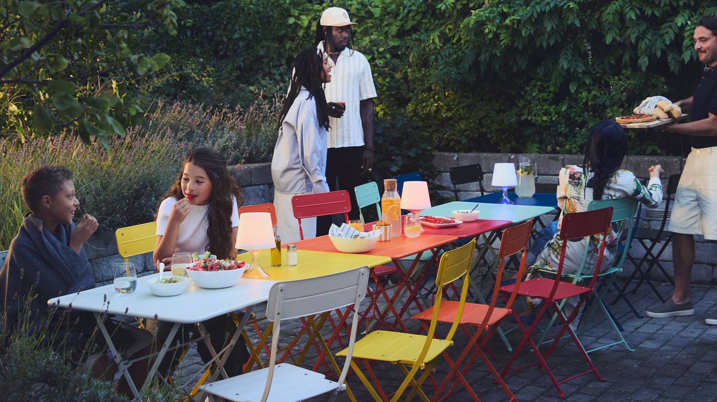 Neighbors gathered in the courtyard around colorful SUNDSÖ tables, arranged into a long red, blue, yellow, and white table.