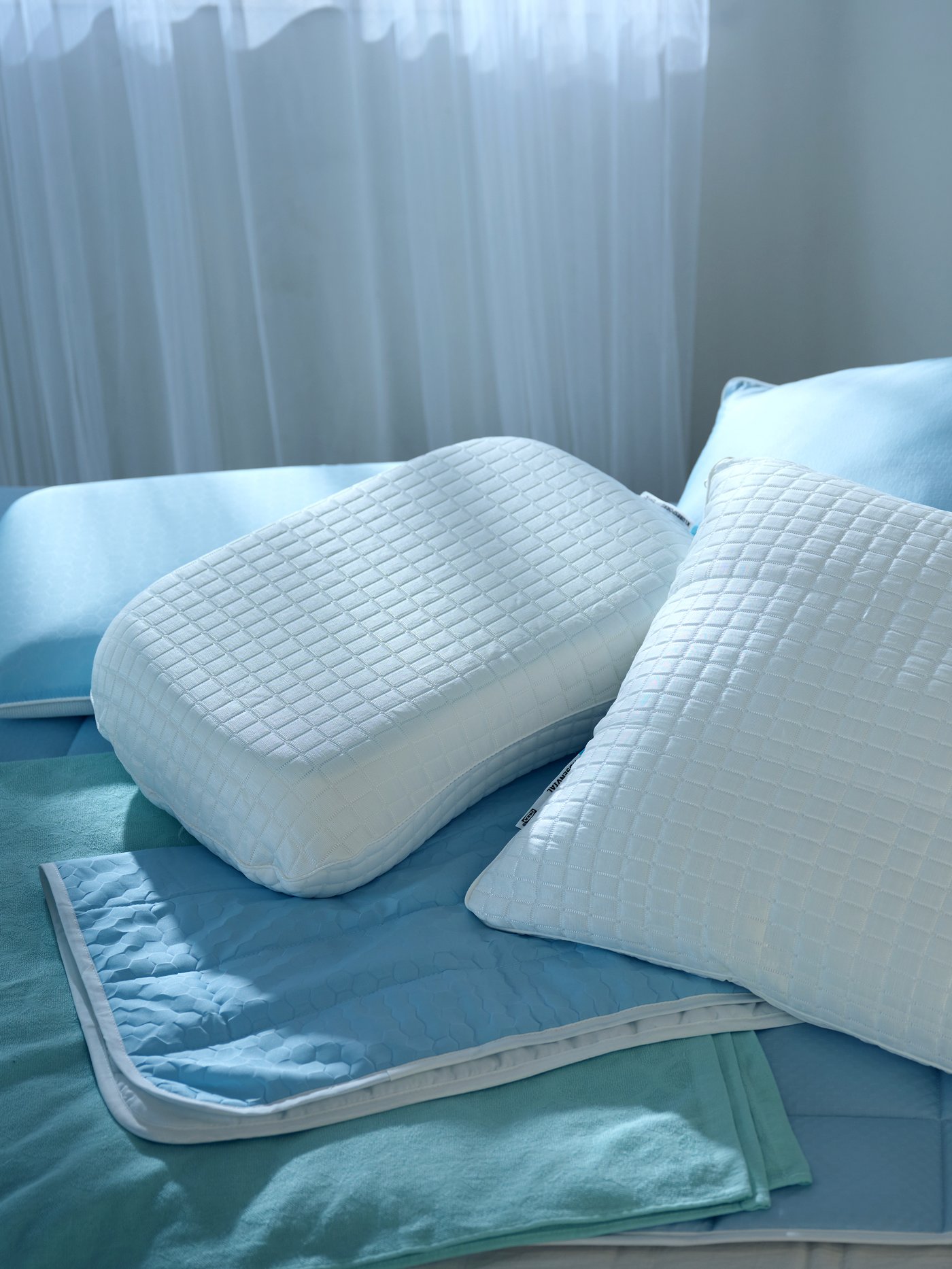 Mehrere Kopfpolster und Kühlunterlagen auf einem Bett.