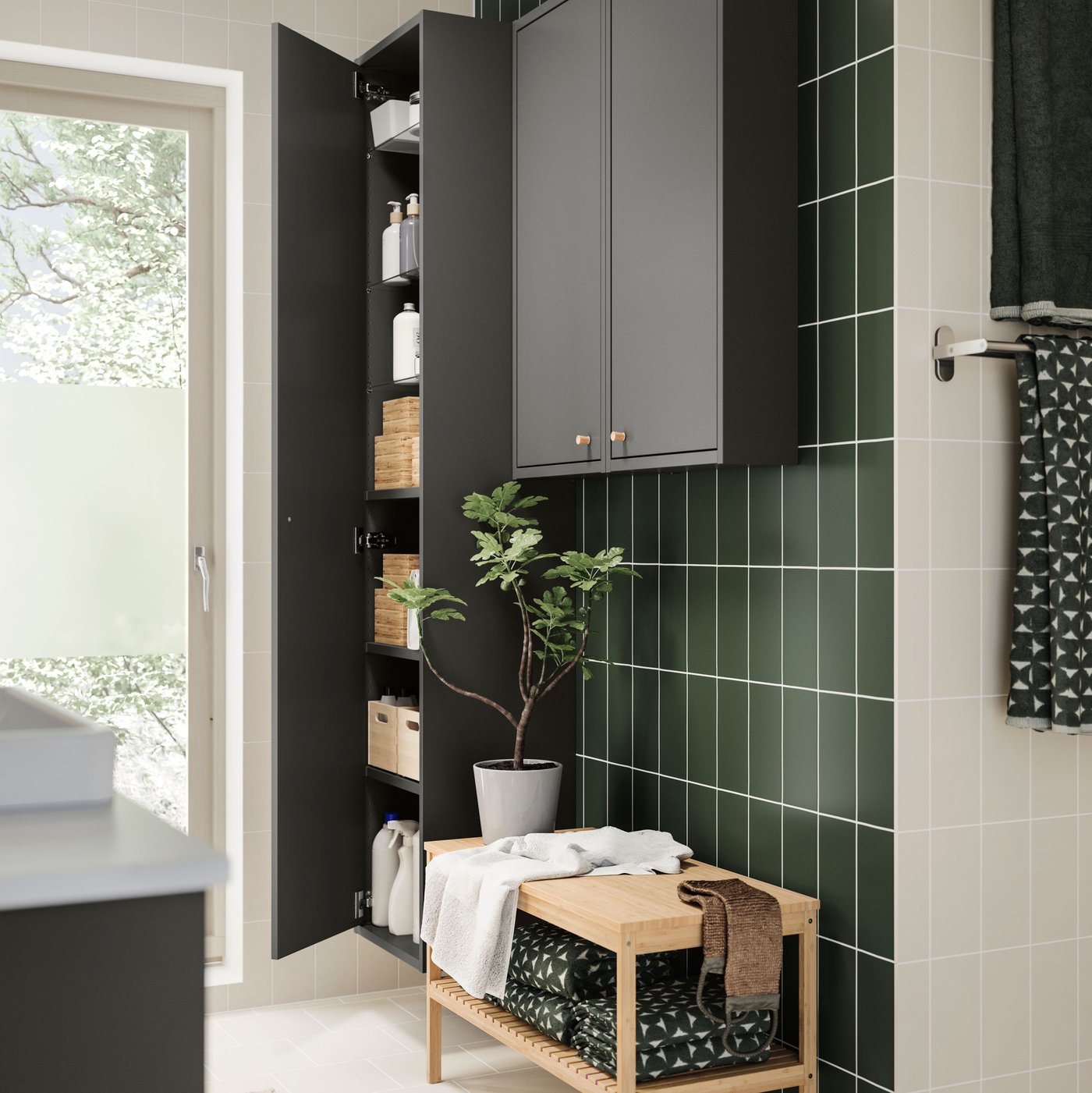 A RÅGRUND bench holding towels and a basket, in front of a tall storage cabinet in a green-tiled bathroom.