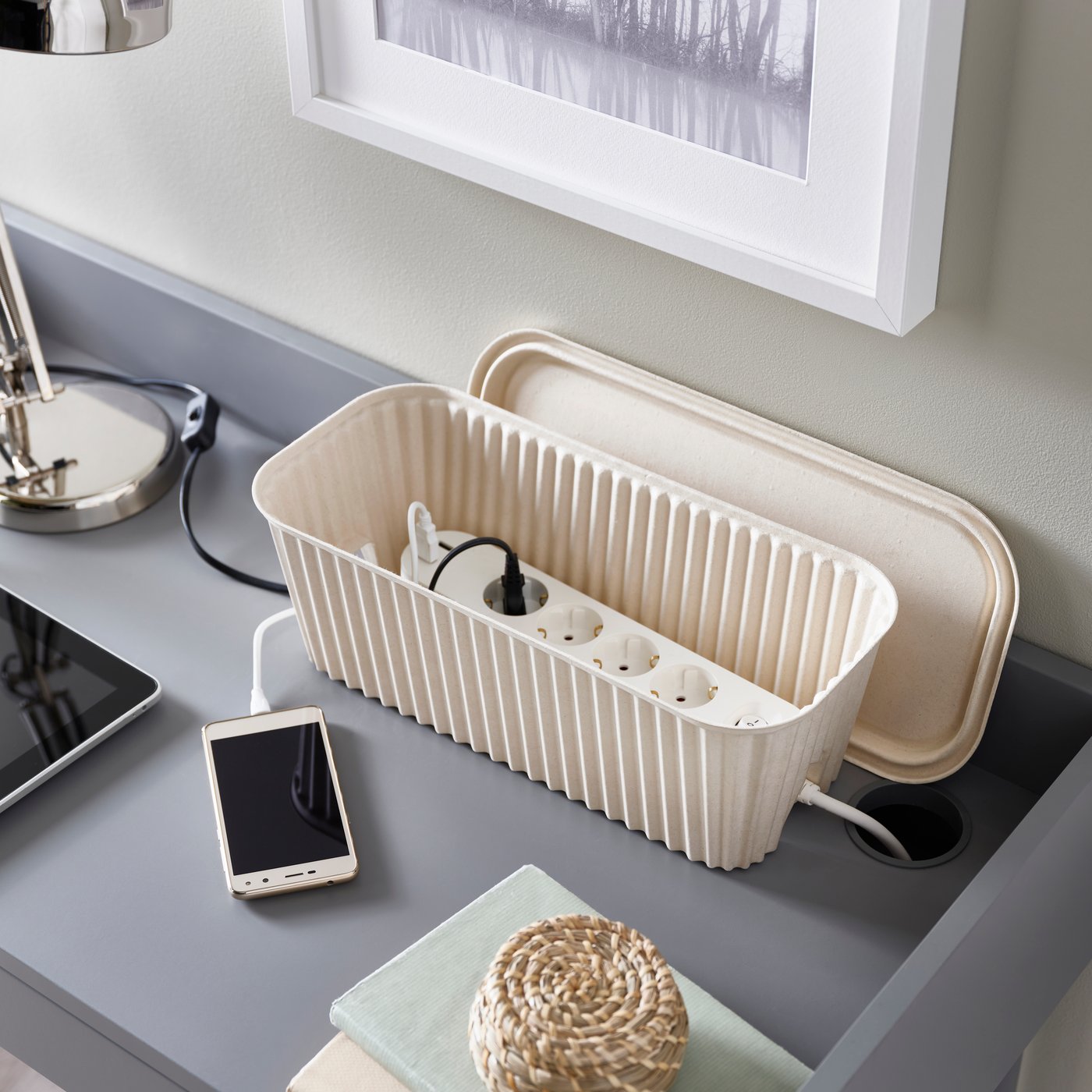 An IKEA HÖNSNÄT cable management box in beige on a grey desk