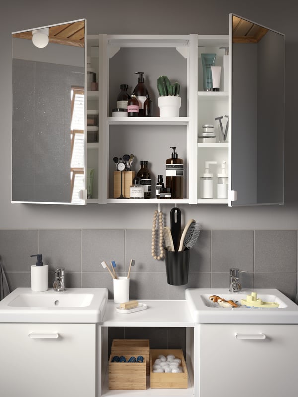 A grey/grey-tiled bathroom with wash-stands and wash-basins in white and a wall cabinet with two mirror doors.