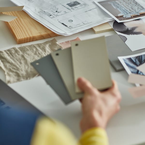 co worker holding a collection of colour swatches with various material swatches on the table in the background