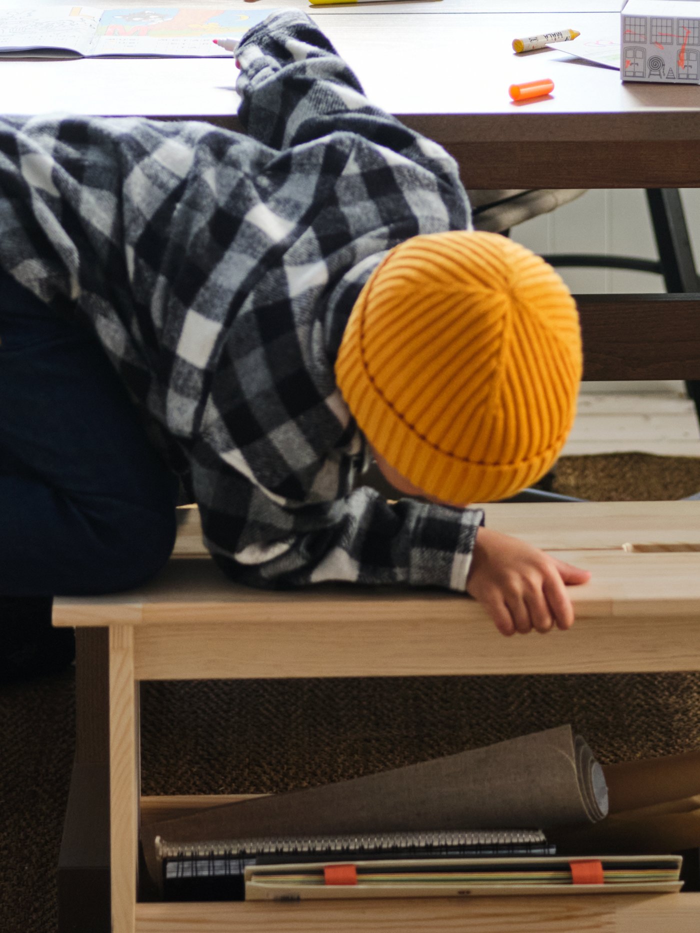 A young boy leaning over the sid of a PERJOHAN pine bench, peering down into its semi-filled storage compartment.