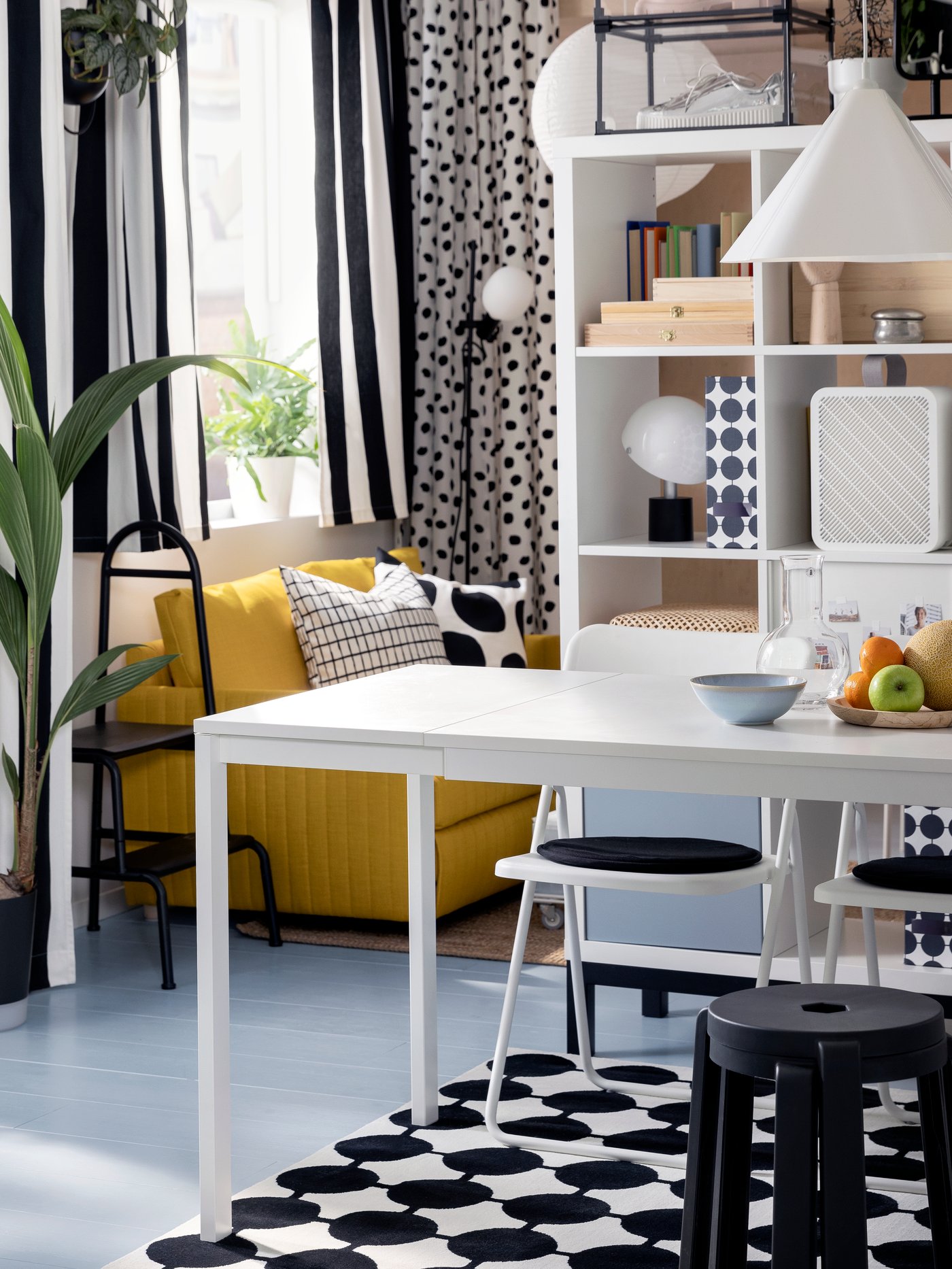 Two stacked, dark gray IBBARBRO stools stand at a white VIHALS extendable table in front of a white KALLAX shelving unit.