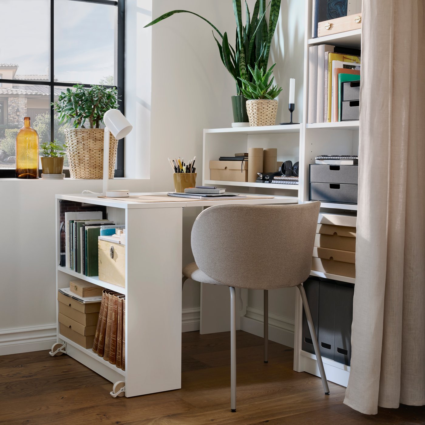 A corner of a bright room with BILLY bookcases, with one section is pulled out to form a desk, filled with desk accessories.
