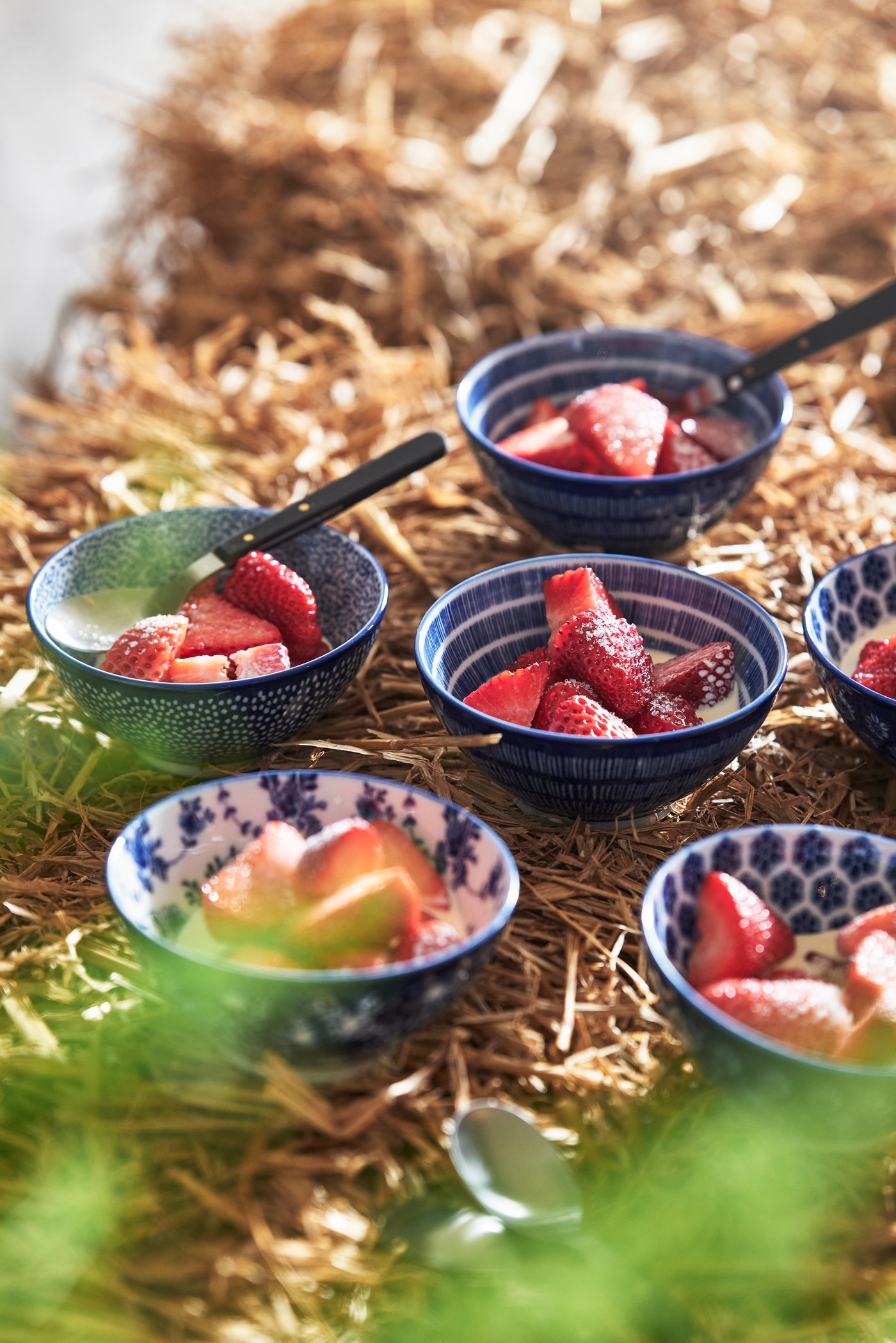 Several ENTUSIASM bowls filled with strawberries on haystacks.
