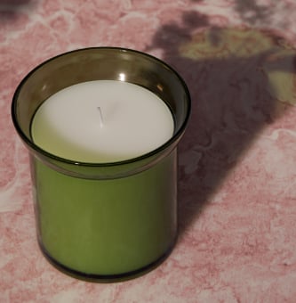 HEDERSAM scented candle in a green glass holder placed on a pink surface.