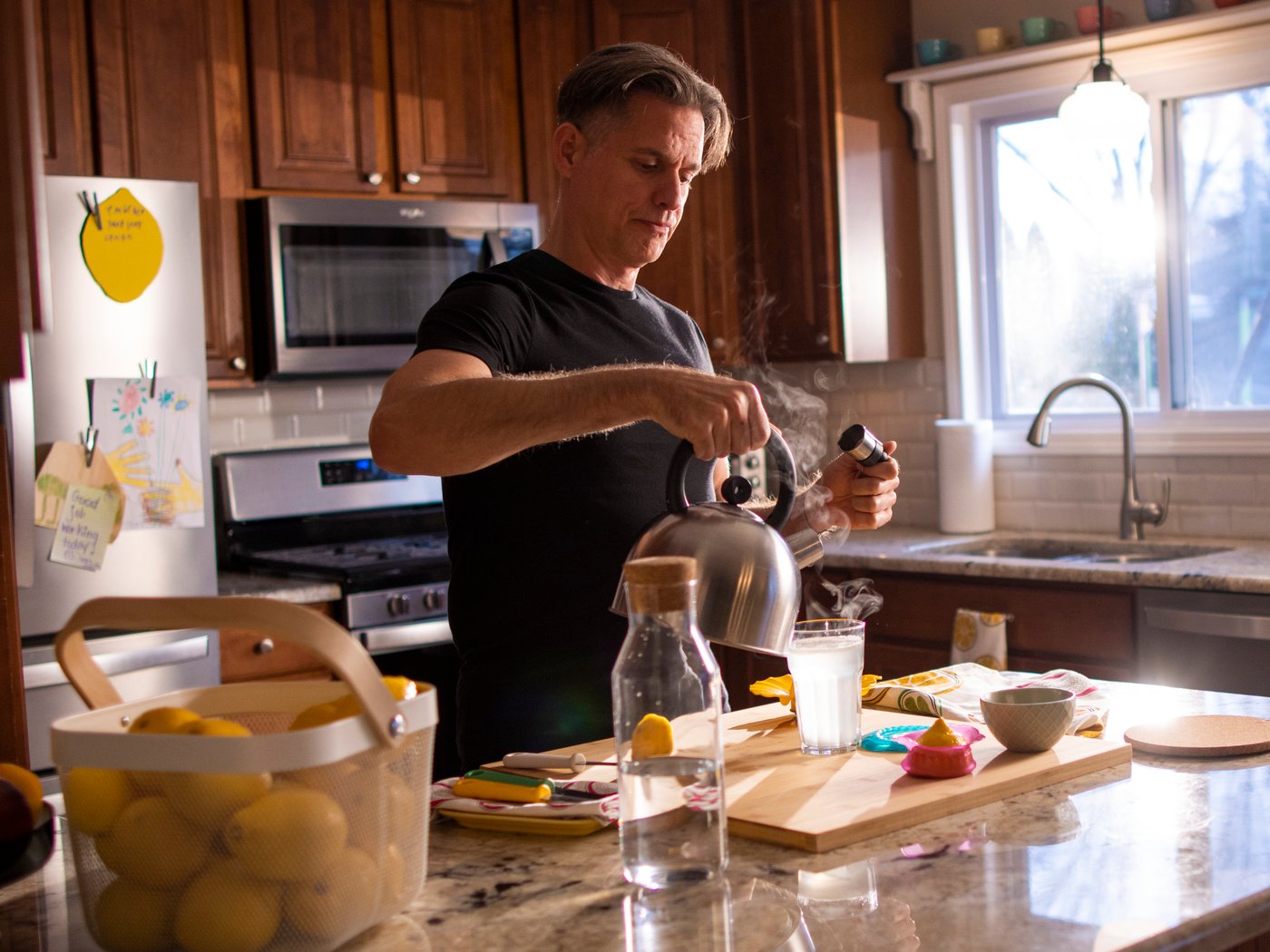 Man preparing a fresh lemon juice drink in a kitchen full of natural light.