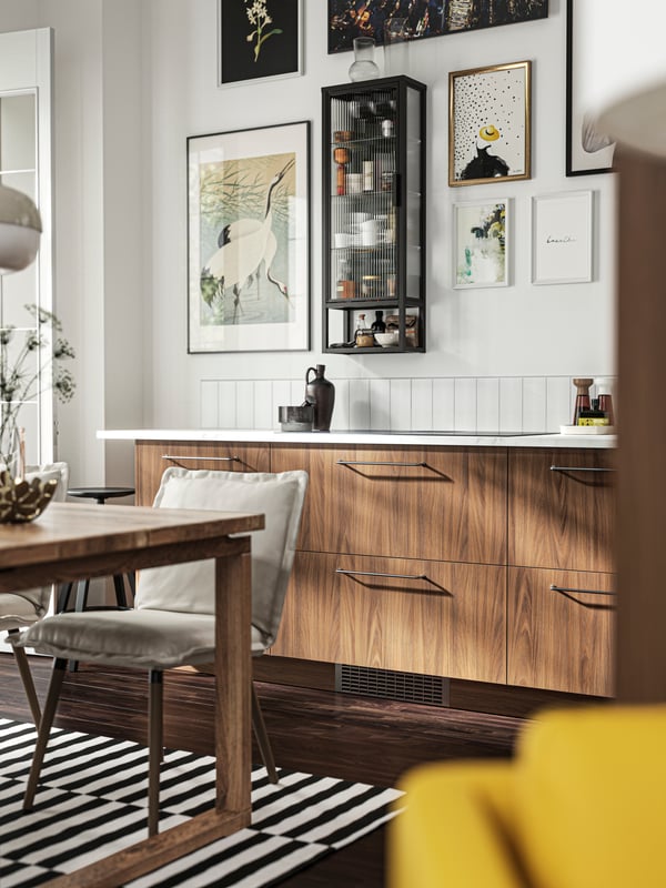 Una cocina con frentes TISTORP con efecto nogal café y un gabinete de pared MOSSJÖN con estantes y puerta de vidrio.