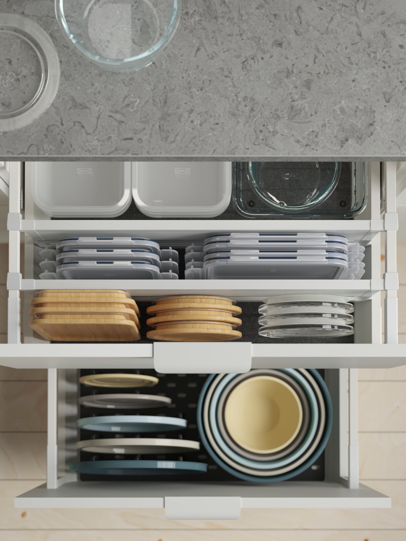 A kitchen cabinet has two drawers, one with drawer dividers and one with a pegboard, where containers and lids are stored.