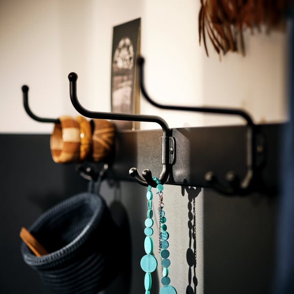 A wall section with necklaces, bracelets and other decorative items hang from a black PINNIG three-hook rack.