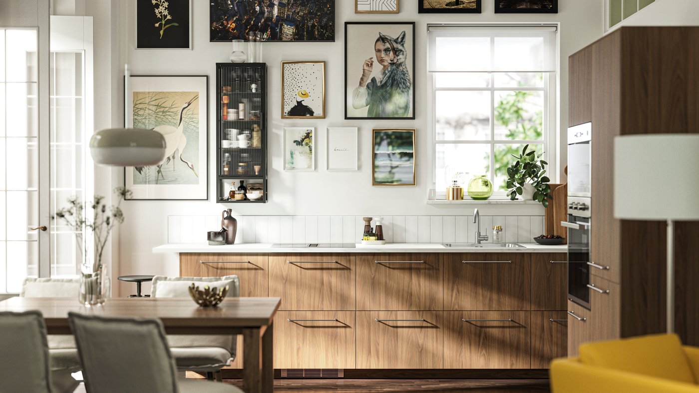 A kitchen with TISTORP fronts with a brown walnut effect, a dark wood floor and some posters on the wall next to a window