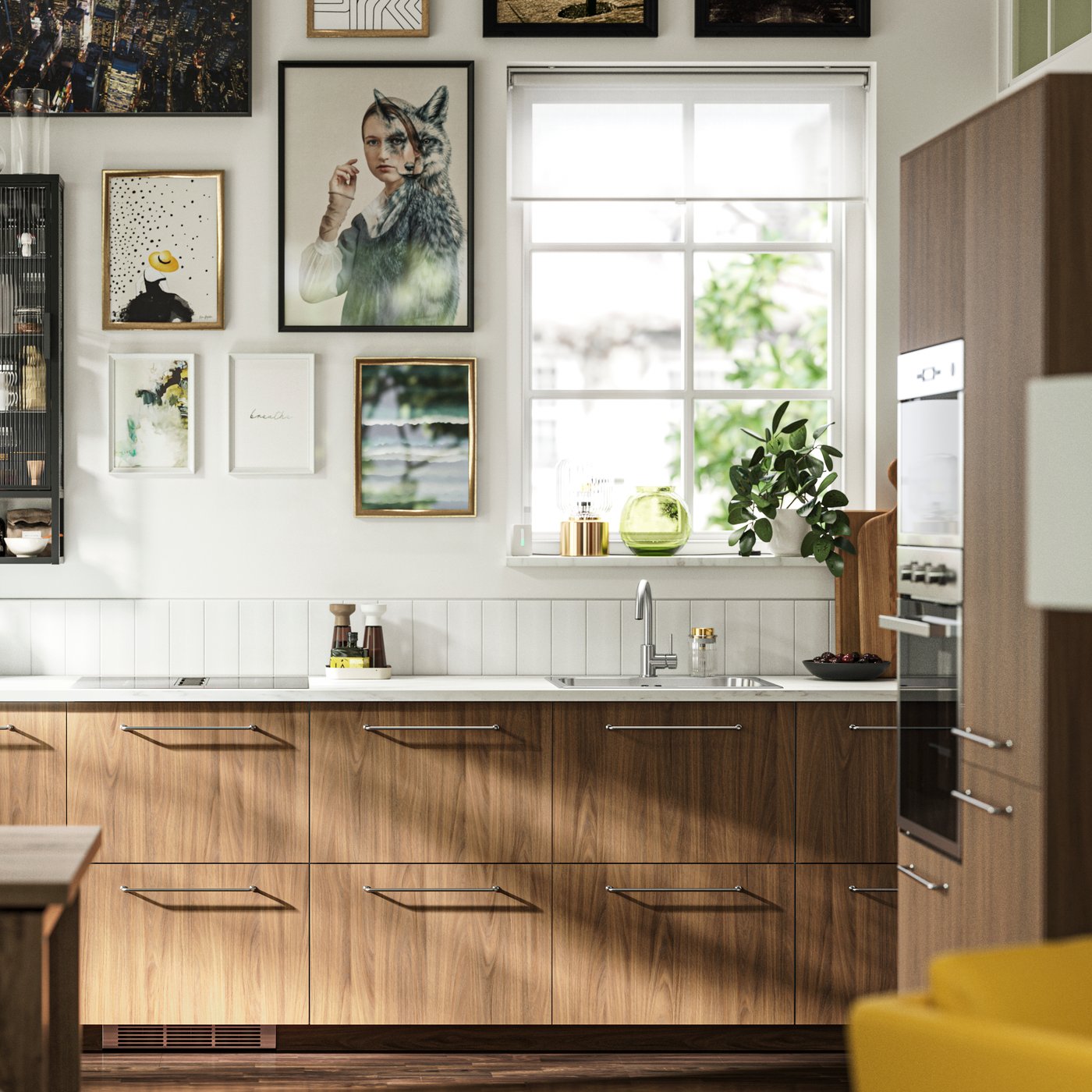 A kitchen with TISTORP fronts with a brown walnut effect, a dark wood floor and some posters on the wall next to a window