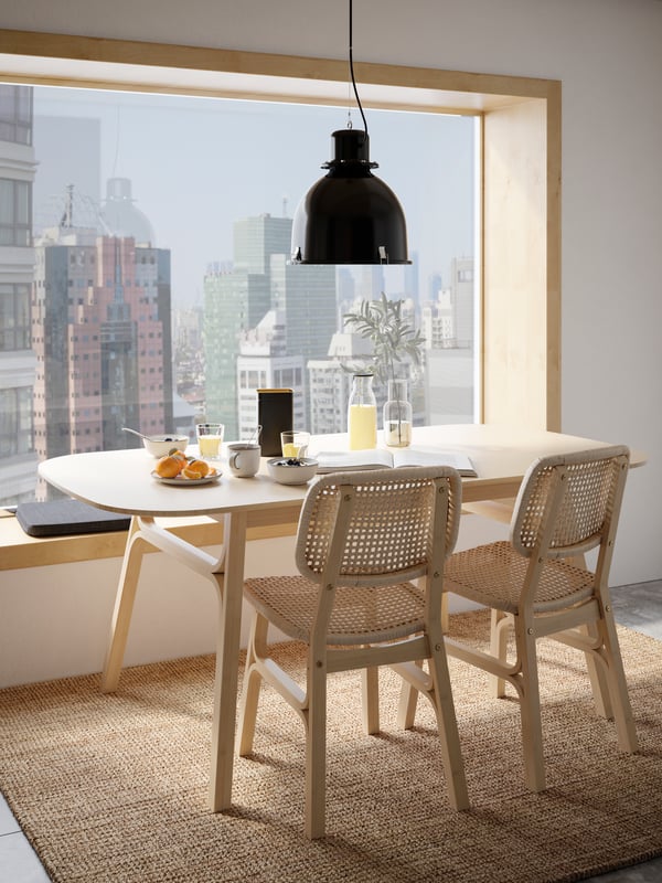 Lámpara de techo negra SVARTNORA industrial sobre mesa de comedor VOXLOV mirando hacia la ventana.