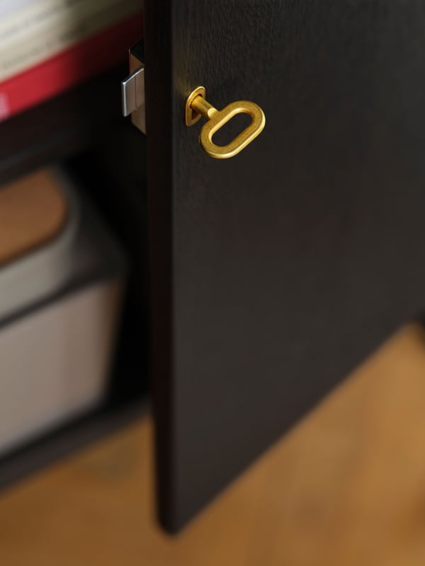 A close-up of a brass-coloured key inserted into an open door of the STOCKHOLM 2025 cabinet with two doors.