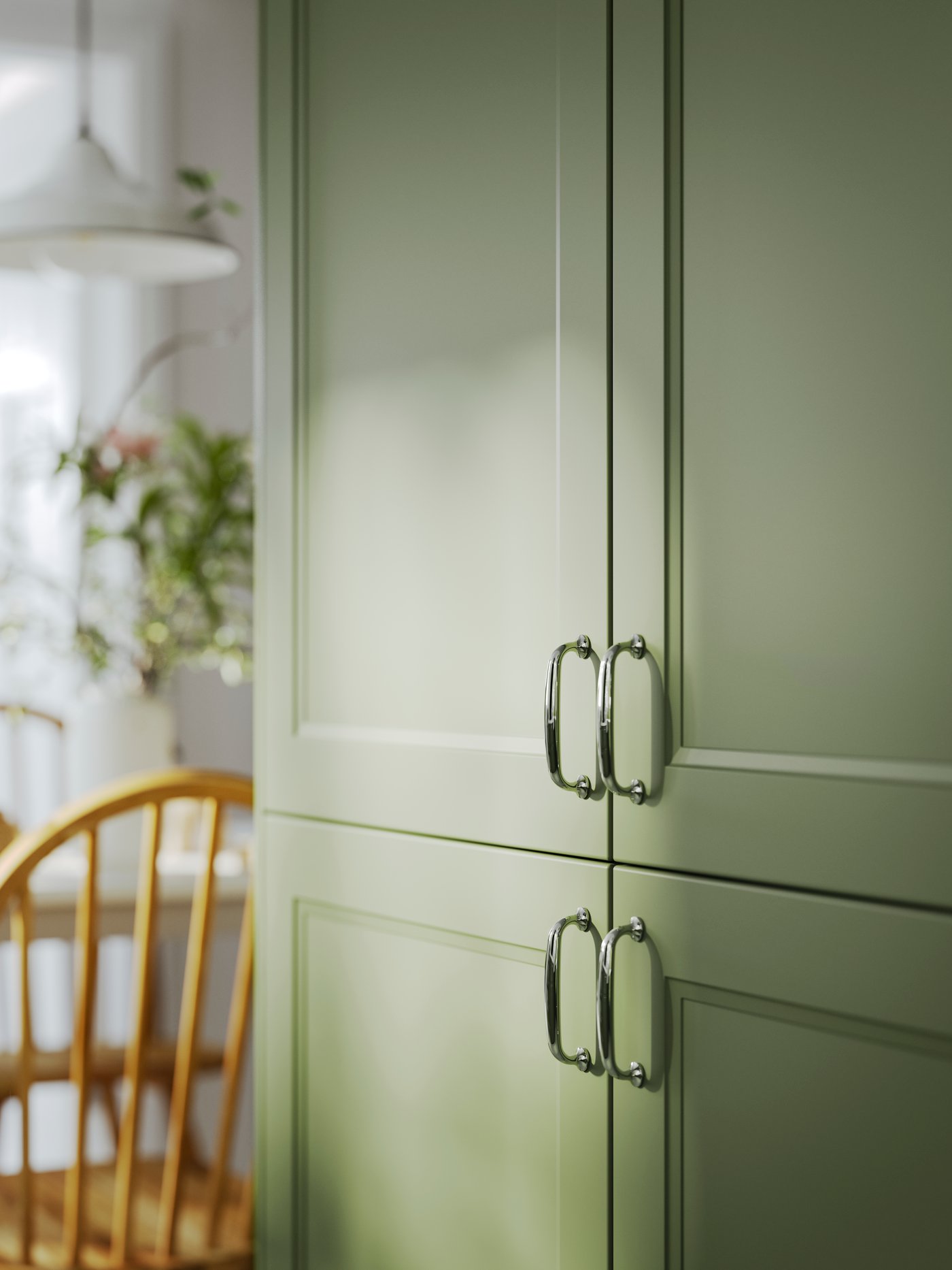 AXSTAD gray-green kitchen cabinet fronts with silver handles, next to a wooden chair and a plant in the background.
