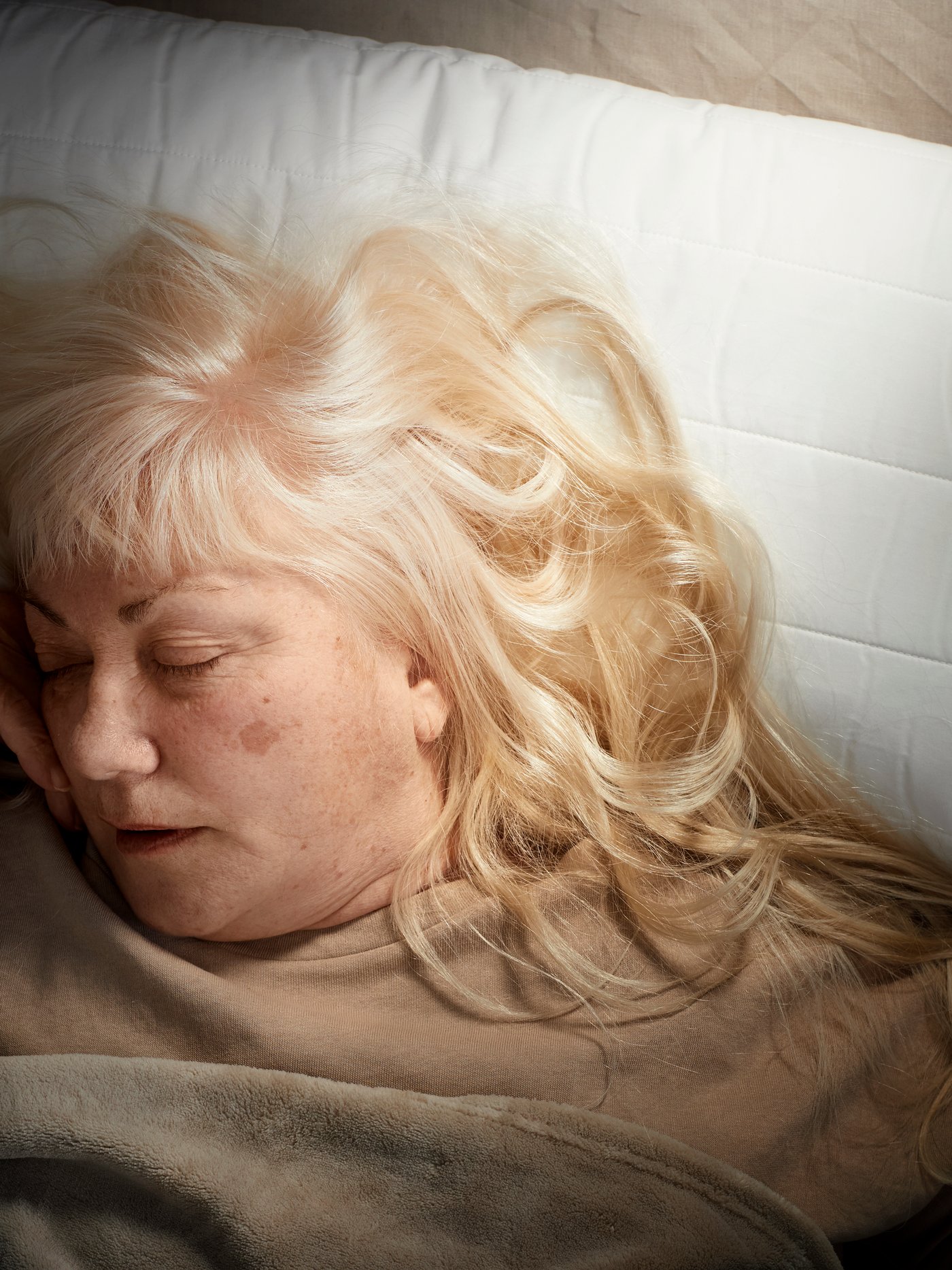 A woman sleeps in a bed with her head on a RUMSMALVA pillow. She has a brown blanket and is wearing a brown top.