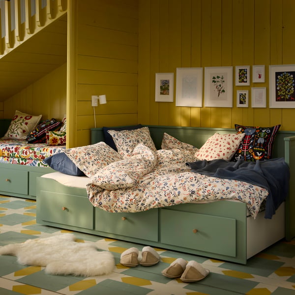 Ein grau-grünes HEMNES Tagesbett mit verschiedenen Decken, Pölstern und Plaids.