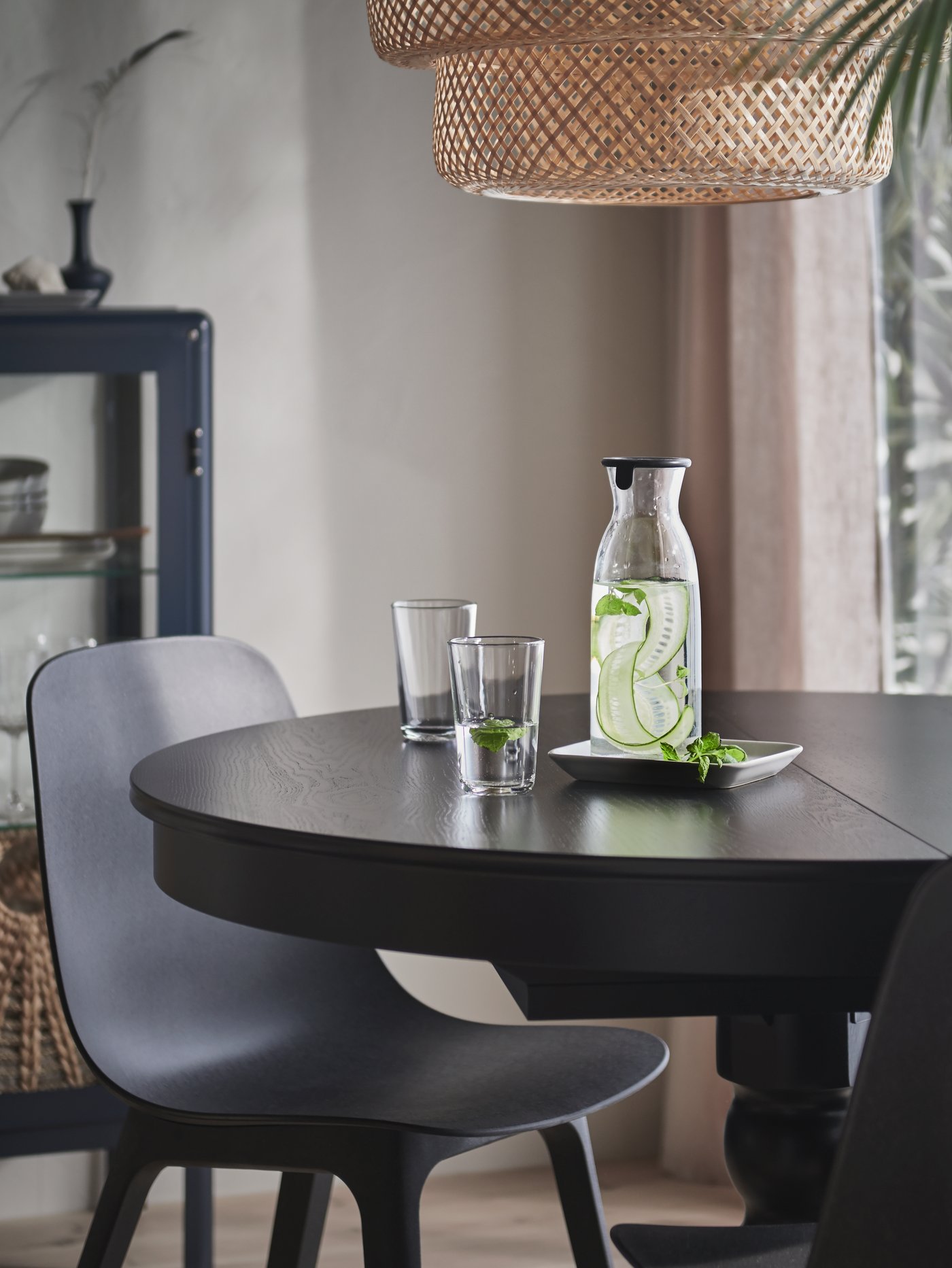 Una mesa de comedor INGATORP negra con una botella de agua y un par de vasos encima. Frente a la mesa una silla ODGER.