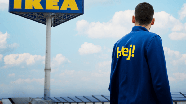 Zaposleni stoj ispred IKEA znaka, okruženog solarnim panelima pod vedrim nebom
